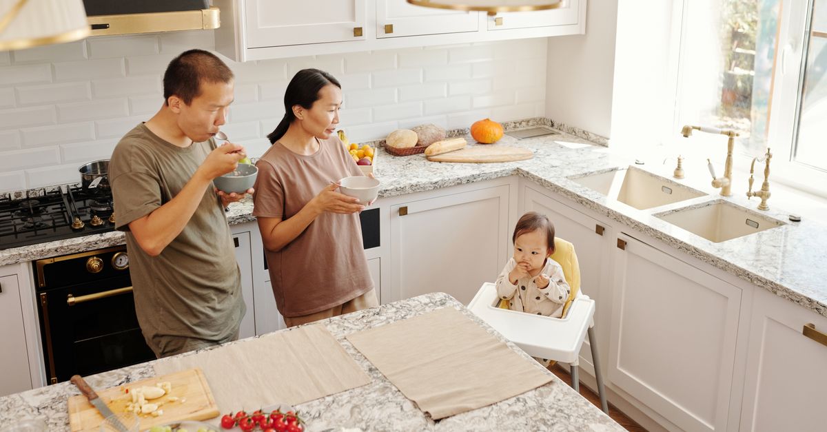 A family of four reviewing a handwritten grocery list at a kitchen table with a laptop open beside them.